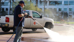 Technician pressure washing pavement near One Stop Property Services truck