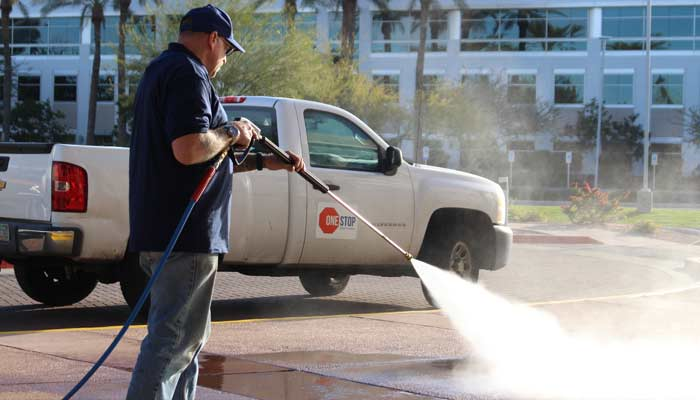 Technician pressure washing pavement near One Stop Property Services truck