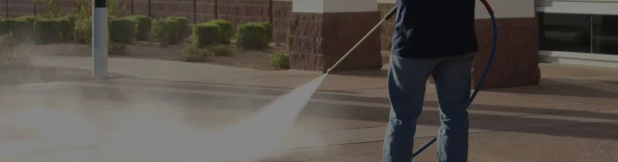 One Stop Property Services technician pressure washing sidewalk near office entrance