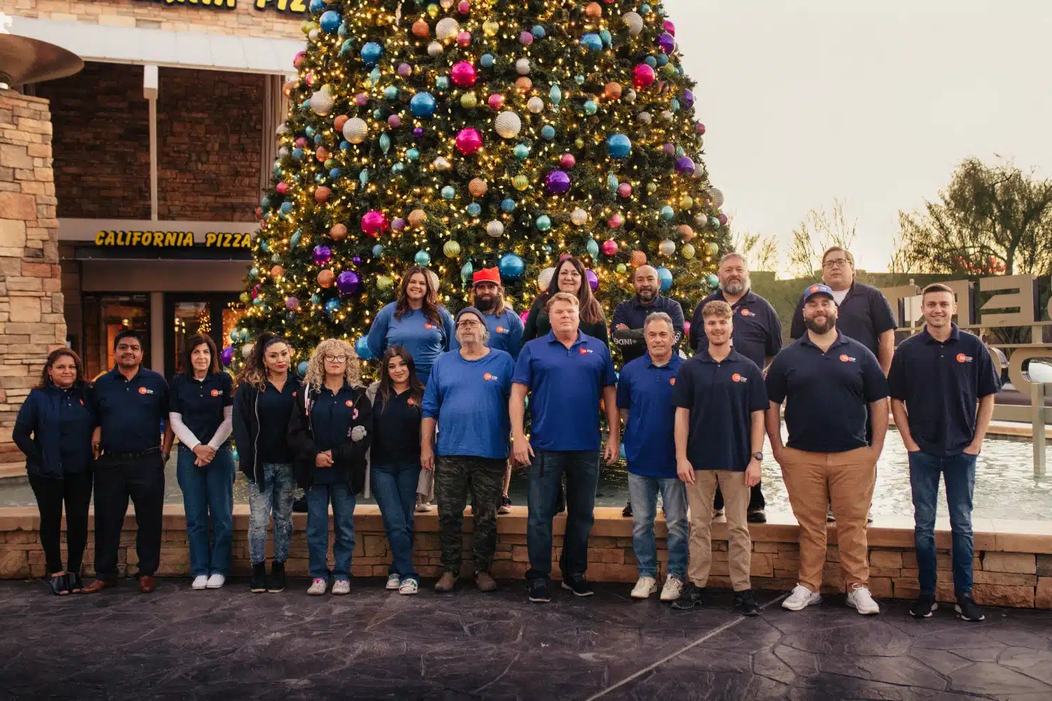 Group photo of One Stop Property Services staff standing in front of a decorated Christmas tree at California Pizza Kitchen